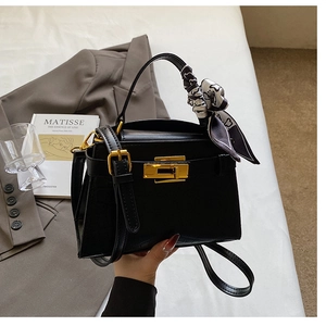 Détail du sac à texture crocodile noir avec boucles dorées et poignée en foulard de soie