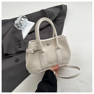 Detail of cream pleated handbag with vertical texture, sturdy handles, and metal snap button