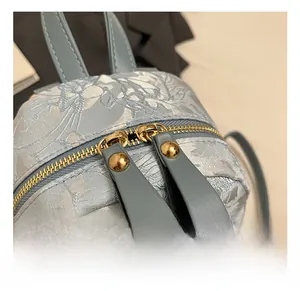 Macro view of golden double zippers and floral jacquard texture on a mini backpack