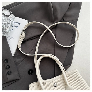 Detail of pleated cream bucket bag with silver metal snap and adjustable strap on a grey suit