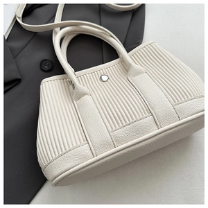 Detail of cream pleated bucket bag with silver clasp and lychee texture stitching