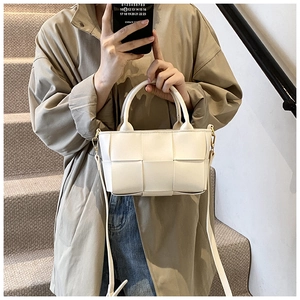 White woven leather crossbody bag with round handle and gold hardware on stairs