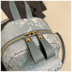 Détail de la broderie papillon et de la texture jacquard florale sur mini sac à dos bleu