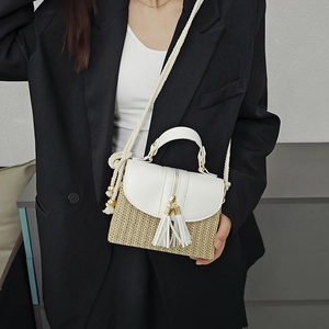Chic woven straw handbag with white leather accents and tassels shown on a model