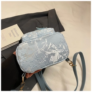 Détail montrant la texture jacquard florale et la poche avant du mini sac bleu clair