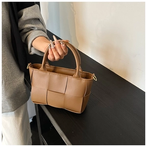 Detailed close-up of brown woven handbag showing large grid texture and gold metal rings