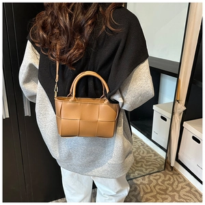 Detail of light brown woven leather crossbody bag with top handles and textured finish