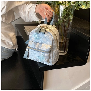 Gros plan d'un mini sac à dos bleu clair avec texture florale et broderie papillon