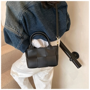 Detail of a black woven crossbody bag with gold hardware and removable shoulder strap