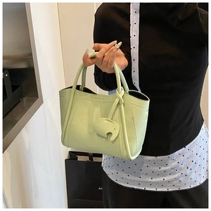 Close-up of light green pebbled leather tote bag with elephant charm and dual handles