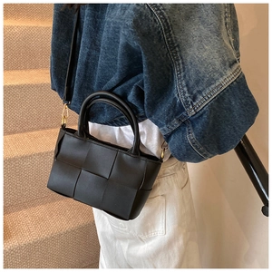 Detail of a black woven crossbody bag featuring a matte finish and rounded top handles