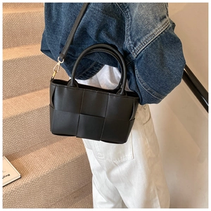 Detail of black woven crossbody bag featuring premium wide leather strips and golden hardware