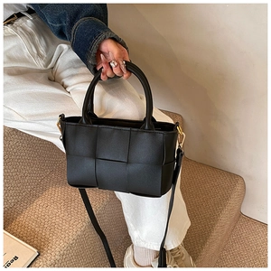 Detail of black woven leather tote bag featuring golden hardware and cylindrical handles