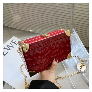Detail of burgundy crocodile-embossed box bag with gold metal corners and chain