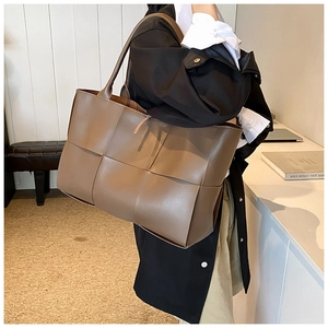 Detailed close-up of brown woven leather tote bag with wide craftsmanship and double straps