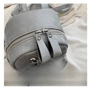 Détail d'un mini sac à dos en cuir PU gris avec double fermeture éclair et pendentif papillon
