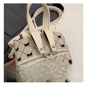 Close-up of embroidered bow pattern on beige checkered mini backpack with silver zipper