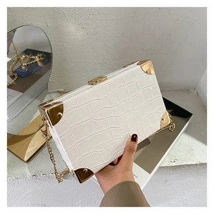 Detail of white crocodile embossed box clutch featuring gold metal corners and chain strap