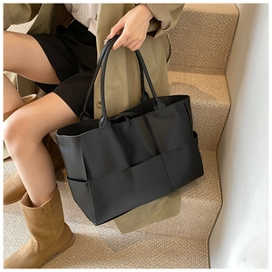 Detail of black woven tote bag featuring soft matte leather and drawstring closure