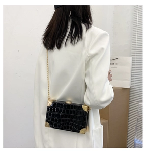 Detail of black crocodile pattern box bag with gold metal corners and chain strap