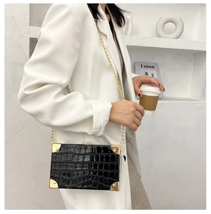Detail of black crocodile texture box bag with gold metal corners and chain strap
