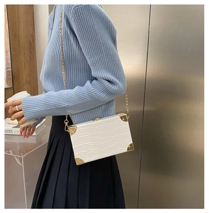 Detailed view of a white crocodile pattern box bag with golden metal corners and chain strap