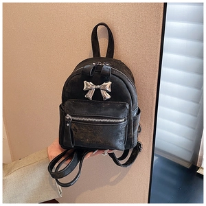 Détail d'un mini sac à dos noir avec texture vintage et décoration de nœud en métal argenté