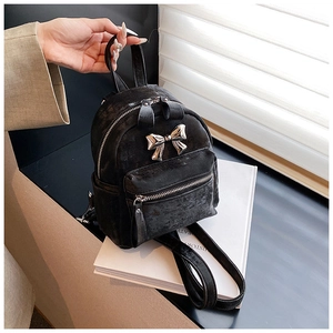 Mini sac à dos noir avec nœud argenté posé sur des livres décoratifs en lumière douce