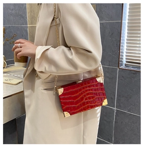 Detail of red crocodile texture box bag with gold chain worn by model in beige suit
