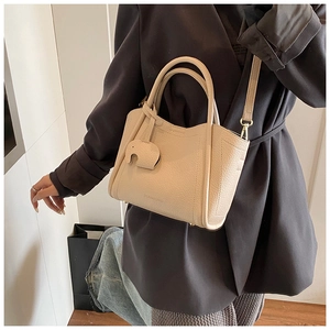 Detail of cream leather bucket bag with elephant charm and branding on charcoal blazer