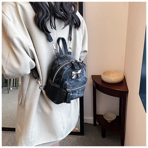 Détail d'un mini sac à dos en velours noir avec nœud métallique argenté porté à l'épaule