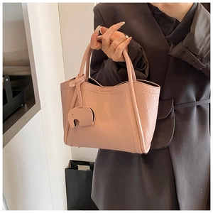 Pink lychee grain leather bucket bag with elephant charm detail held by a model