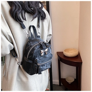 Détail d'un mini sac à dos noir avec un nœud métallique vintage et des zips à franges