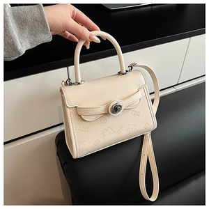 Dettaglio del rilievo con orsetto e torta su un'elegante borsa a tracolla in pelle crema
