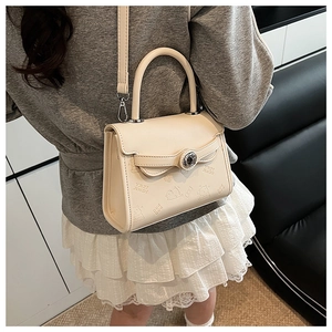 Detail of cream square crossbody bag featuring embossed bear pattern and metal clasp