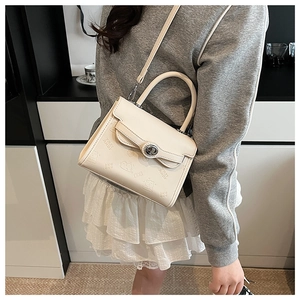 Close-up of embossed cartoon patterns and metal lock on cream-colored small square bag