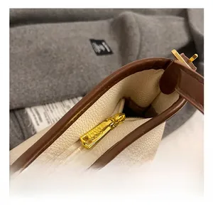 Gros plan sur la fermeture éclair dorée et le cuir crème texturé du sac fourre-tout
