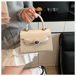 Close-up of cream leather handbag with embossed cartoon pattern and silver twist lock
