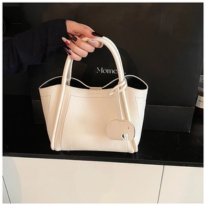 Close-up of white lychee pattern leather bucket bag with elephant charm and U-shaped stitching