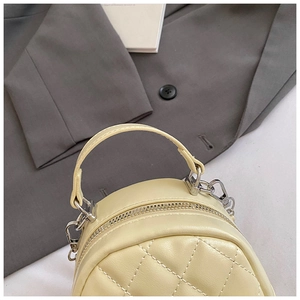 Detail of light yellow quilted PU leather handbag with silver metal buckles and stitching