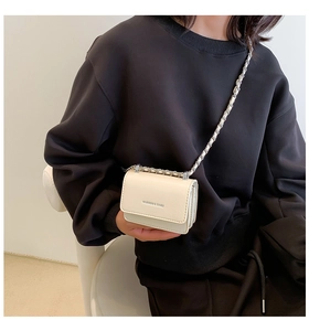 Dettaglio mini borsa a tracolla bianco crema con catena d'argento su maglia nera