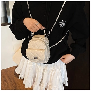 Detail of beige quilted backpack with chain strap and metallic clasp on model