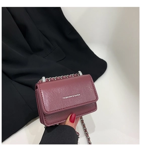 Dettaglio mini borsa fucsia con catena e scritte argento tenuta in mano dalla modella