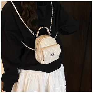 Detailed side view of a white quilted patent leather mini backpack worn by a model