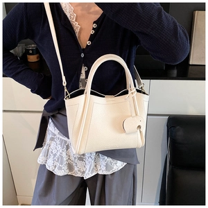 Detail of cream white bucket bag with elephant charm on model in modern interior