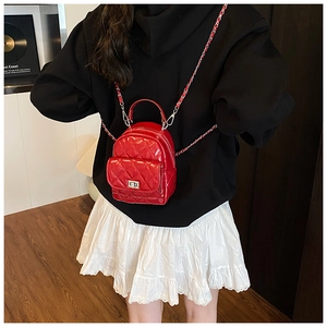 Detail of red quilted mini backpack featuring glossy finish and chain straps on model