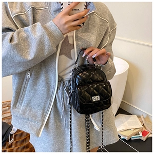 Detail of a black quilted mini backpack with metallic chain straps on a lifestyle model