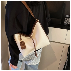 Gros plan d'un sac cabas en cuir crème avec bordures brunes porté par un mannequin