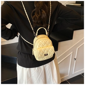 Rear view of a model wearing the cream yellow quilted mini backpack with chain straps