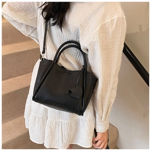 Detail of black pebbled leather bucket bag with cute elephant charm and metal base studs